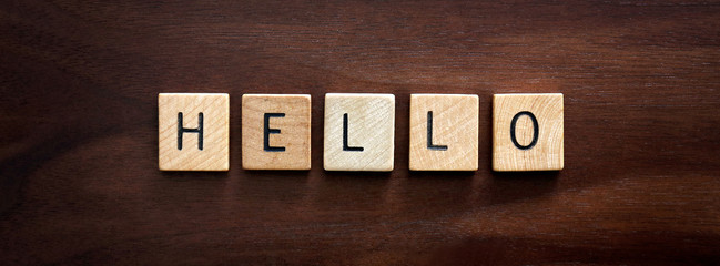 Words Hello Spelled out in Wooden Letter Blocks on Dark Walnut Wood Background.