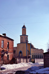 Fototapeta na wymiar Mosque building, soft yellow colors with moons on top, on old city street in winter, red brick building with snow on roof, blue sky background, Kharkiv, Ukraine