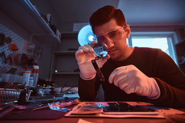 Electronic technician mending a broken tablet carefully examines the chip of the tablet using a...