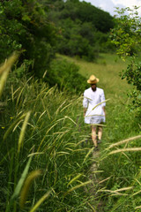 A young woman in a white dress and hat is walking along the path among the green grasses