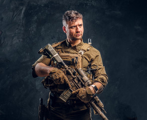 Special forces soldier wearing body armor holding assault rifle. Studio photo against a dark textured wall