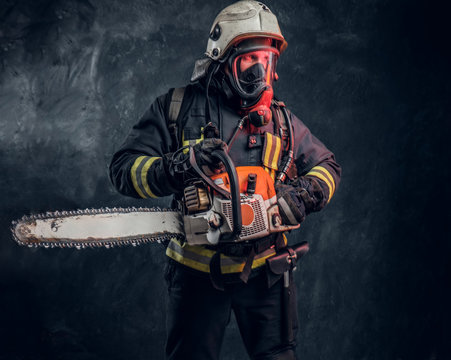 Firefighter in safety helmet and oxygen mask holding a chainsaw. Studio photo against a dark textured wall