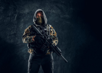 Special forces soldier in military uniform wearing mask and hood holding an assault rifle. Studio...