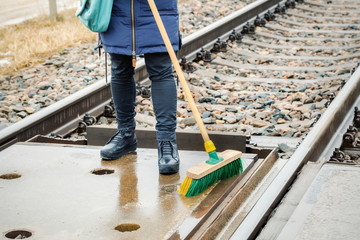Woman railway employee clean with brush railway crossing
