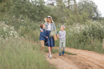 Mother in a straw hat, denim dress with young sons walking through the woods .Outdoor spring leisure concept