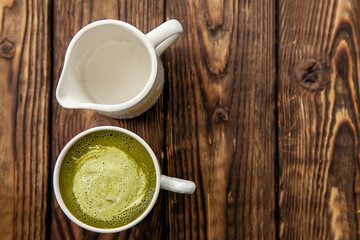 cup of hot matcha green tea latte and cup of milk on wood background