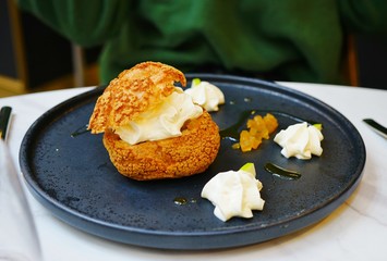 A craquelin choux pastry cream-puff dessert filled with cream on a black plate