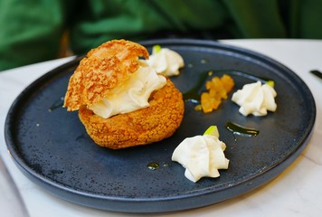 A craquelin choux pastry cream-puff dessert filled with cream on a black plate