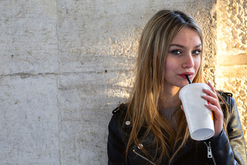 Young stylish woman drinking coffee to go in a city street 