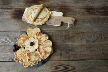 pancakes in the shape of a heart and flowers and pancakes on a board on a rustic wooden table with space for text. Shrovetide, carnival concept.