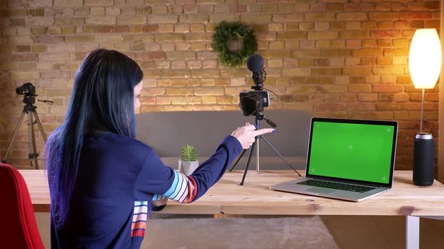 Closeup shoot of young attractive caucasian female video blogger streaming talking on camera and having a lapop with green screen in front of her