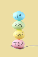 Female hand holds a spoon on which multi-colored eggs are balanced, on a yellow background. Unusual design, Easter concept, copy space.