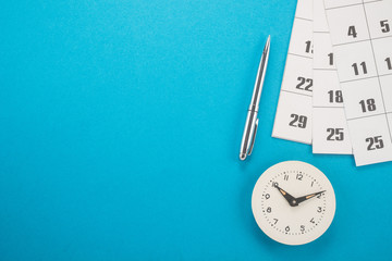 Fototapeta na wymiar Calendar with dates, clock and pen on blue background