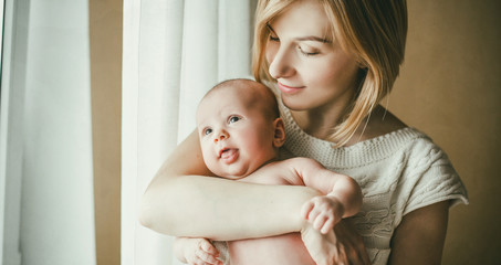 newborn baby in a tender embrace of mother at the window
