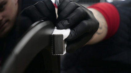 A professional worker guy (Male) applies ceramics (special liquid) to the car using an applicator (sponge) in black gloves and in a protective robe. Concept of: Auto service, Deteyling.