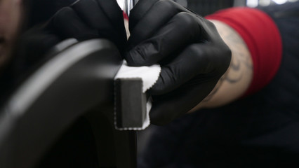 A professional worker guy (Male) applies ceramics (special liquid) to the car using an applicator (sponge) in black gloves and in a protective robe. Concept of: Auto service, Deteyling.