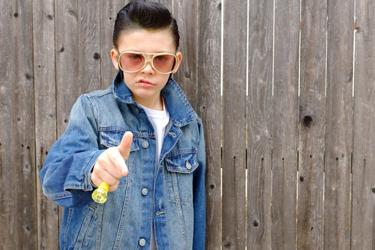 Elvis kid,Boy child dressed as 1950s style greaser ,rockabilly wearing denim jacket with pompadour slicked back ,jet black hair. 