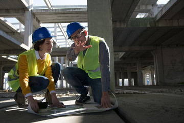 Fototapeta na wymiar Two industrial engineer kneeling on the floor and discussing over blueprint
