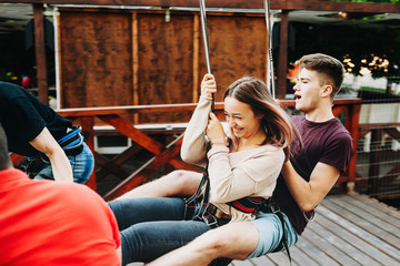 Obraz premium Young cute extreme couple rope sliding and gaining speed on the ropeway where girl is laughing with fear and man is screaming both holding by rope slide cable.