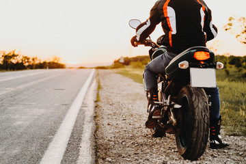 Crop view of a biker on his bike from back while traveling preparing to start near the road against sunset in his adventure time.