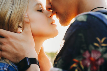 Fototapeta Close up portrait of a cute young caucasian blonde couple trying to kiss where man is holding his girlfriend face in his hands close outside while dating. obraz