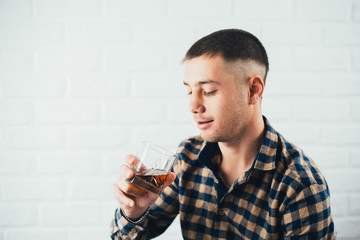 Young businessman with a glass of whiskey and a white brick wall