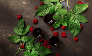 Homemade raspberry liqueur with fresh berries decorated green leaves, brown table background, top...