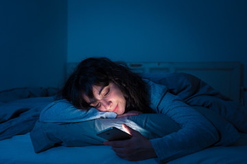 Fototapeta na wymiar Attractive latin woman addicted to mobile phone and internet late at nigh in bed looking sleepless