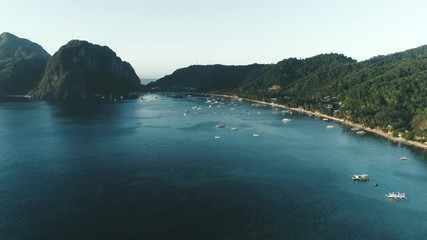 Aerial drone view of boats anchored in the bay with clear and turquoise water on the sunset. Boat and yacht in the tropical lagoon. Tropical landscape. El Nido, Palawan island, Philippines.