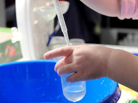 Kid doing scientific experiment at home with liquids holding a test tube and a pasteur pipette. Hands close-up, the concept of early development.