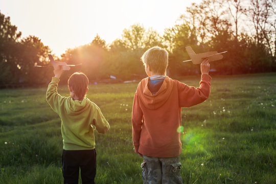 A boy in a green jacket runs across the field at sunset. The child launches a paper airplane. Happy childhood. Walking on the street without a phone.