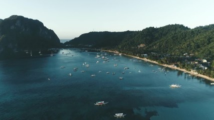 Aerial drone view of boats anchored in the bay with clear and turquoise water on the sunset. Boat and yacht in the tropical lagoon. Tropical landscape. El Nido, Palawan island, Philippines.