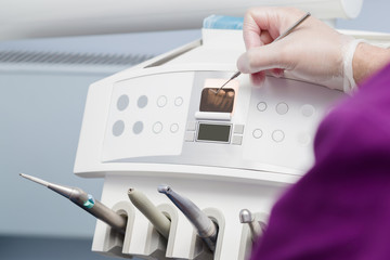 Dentist's hands in rubber protective gloves with tool pointing to x ray of teeth on display. Dental equipment monitor in office. Closeup.