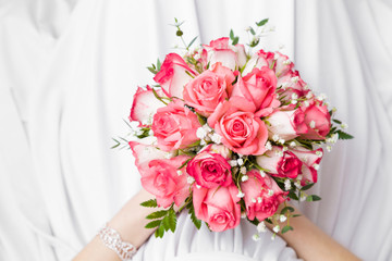 Pink roses bouquet in bride's hands on lap. White wedding dress. Point of view shot. Closeup. 