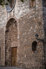 an ancient part of the building, a wall made of stones; arched niche with massive wooden doors above the round window niche