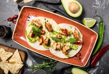 Mexican taco dish with shrimps, bell peppers, tomatoes and chili peppers on a concrete gray background