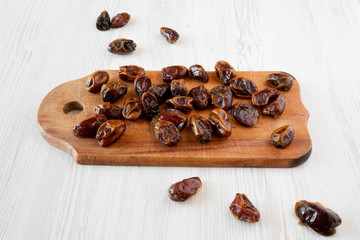 Dried dates on rustic wooden board over white wooden surface, low angle view. Close-up.