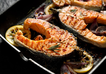 Grilled fish, grilled salmon steak  with addition of lemon, rosemary, garlic, onion and spices on grill plate, top view. 