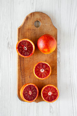Whole and halved blood oranges on rustic wooden board over white wooden surface, top view. Flat lay, overhead, from above.