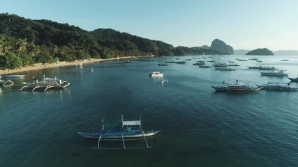 Aerial drone view of boats anchored in the bay with clear and turquoise water on the sunset. Boat and yacht in the tropical lagoon. Tropical landscape. El Nido, Palawan island, Philippines.