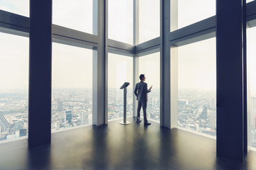 Fototapeta na wymiar Business man stand by glass window in tall building with background of city