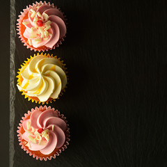 Pink and yellow cupcakes against a black background, birthday or party cupcakes. Party sweet food, desserts. Copy space. Square image.