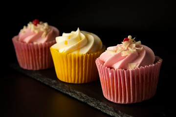 Pink and yellow cupcakes against a black background, birthday or party cupcakes. Party sweet food, desserts. Copy space.