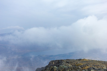 A view from a mountain summit with a loch in the valley and altitude white clouds