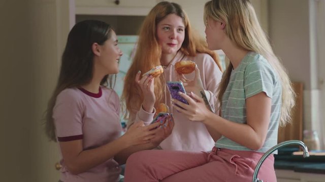 funny teenage girls posing with donuts taking photos using smartphone sharing on social media enjoying hanging out on weekend in kitchen