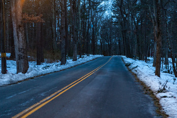 Fototapeta premium Acton, United States, February 27, 2019. Forest road with double yellow line in winter time, Massachusetts, United States