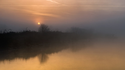 Fototapeta na wymiar fiume con argine all'alba con nebbia del primo mattino