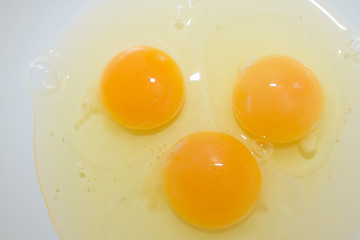 Three broken chicken eggs in a white mixing bowl