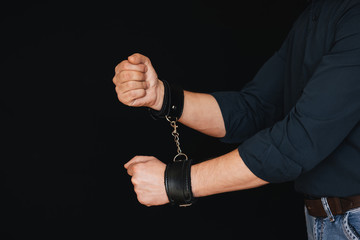 men's hands chained in leather handcuffs on black background