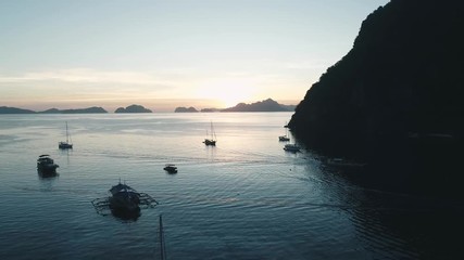 Aerial drone view of boats anchored in the bay with clear and turquoise water on the sunset. Boat and yacht in the tropical lagoon. Tropical landscape. El Nido, Palawan island, Philippines.